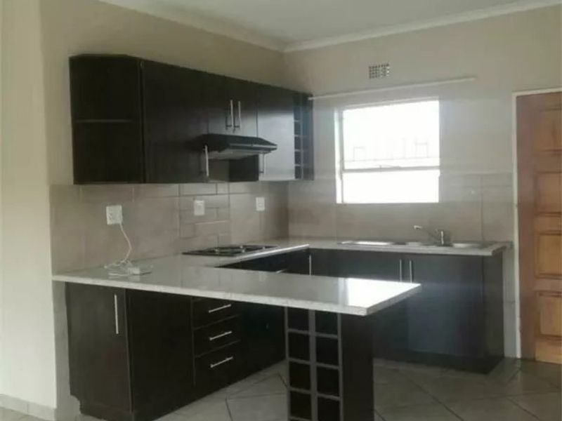 A functional kitchen featuring dark wood cabinetry, stone countertops, a built-in hob with extractor fan, and a convenient breakfast bar with integrated wine storage.