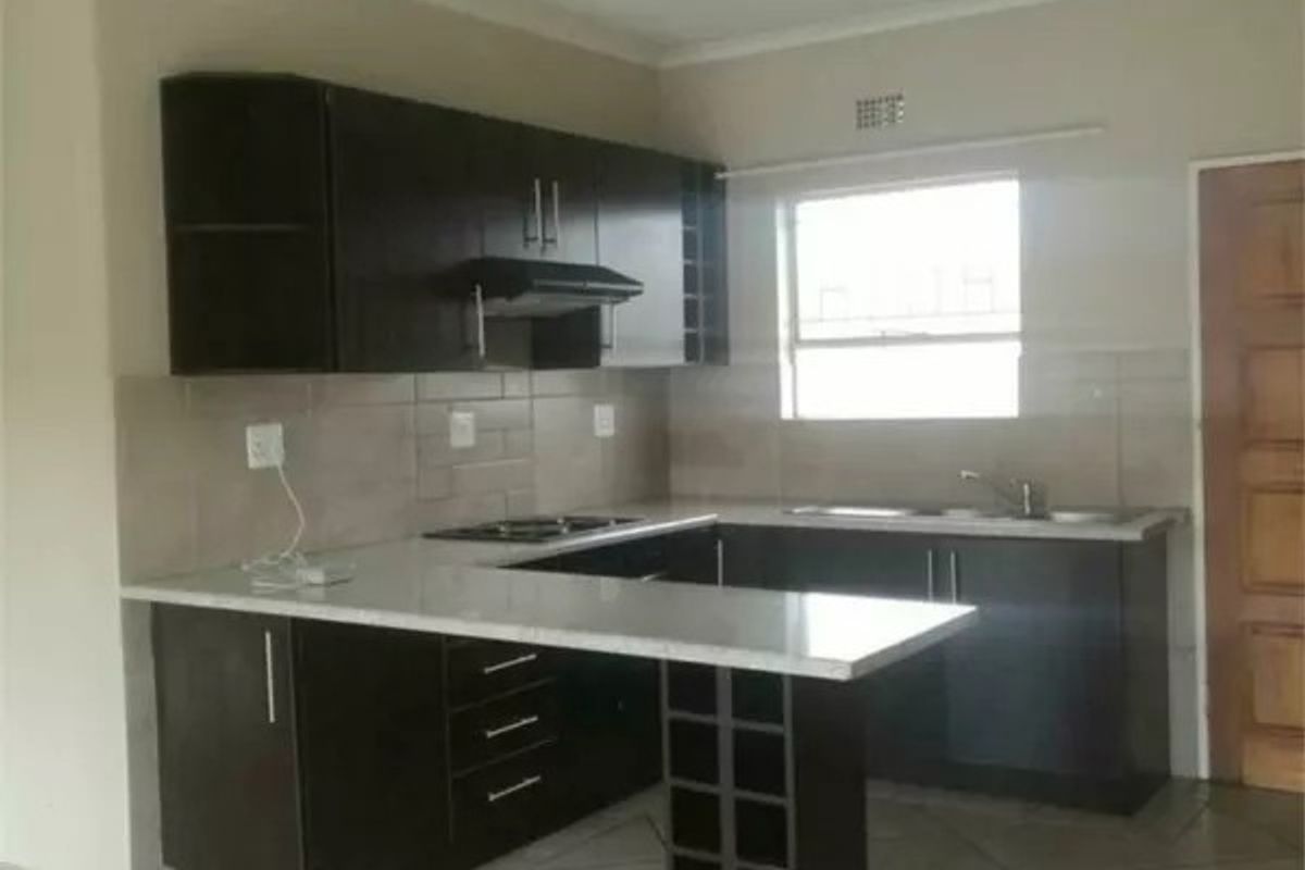 A functional kitchen featuring dark wood cabinetry, stone countertops, a built-in hob with extractor fan, and a convenient breakfast bar with integrated wine storage.