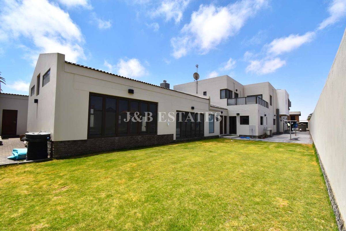 Rear view of the property featuring a spacious lawn, modern architectural design, large windows, and an upper-level balcony.