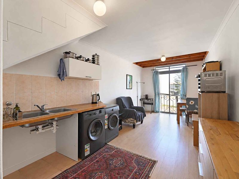 Open-plan living area featuring a kitchenette with double sink, tiled splashback, and direct access to a balcony through sliding glass doors.