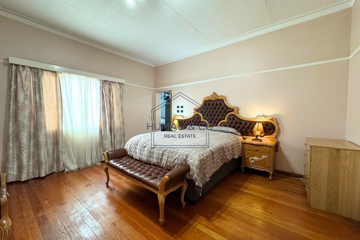 Spacious bedroom featuring polished timber flooring, high ceilings with decorative cornice, and large windows allowing for natural light.