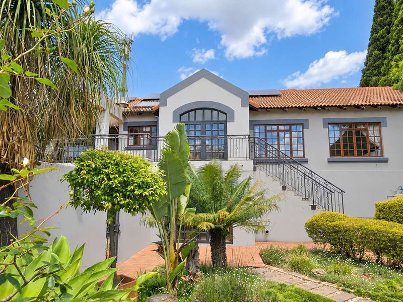 A well-maintained rear exterior view featuring a terracotta tiled roof, wrought iron balcony railings, an external staircase, and a landscaped garden area.