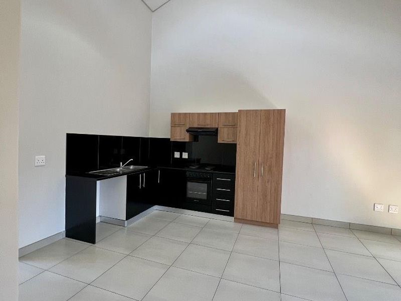 Modern open-plan kitchen featuring sleek black cabinetry, wood-tone accents, built-in appliances, and high vaulted ceilings with tiled flooring throughout.