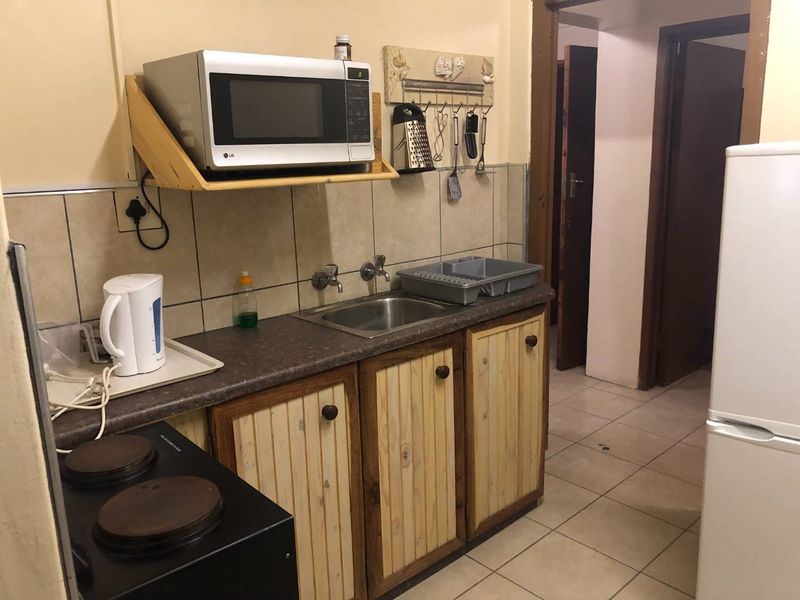 A compact kitchen featuring wooden cabinetry, a stainless steel sink, tiled backsplash, and an electric stove, offering a functional but dated preparation space.