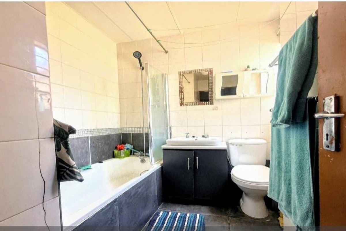 A functional bathroom featuring a built-in bathtub with shower attachment, vanity basin, and toilet, finished with tiled walls and flooring.