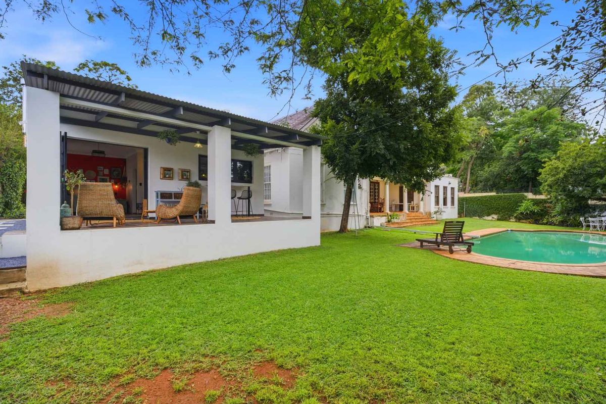 Rear view of the property featuring a covered patio area, a well-maintained lawn, and a swimming pool set within a landscaped garden.