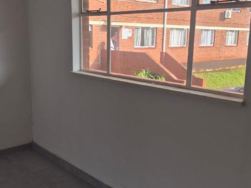 An empty living area featuring tiled flooring and a large window providing natural light and views of the surrounding apartment complex.