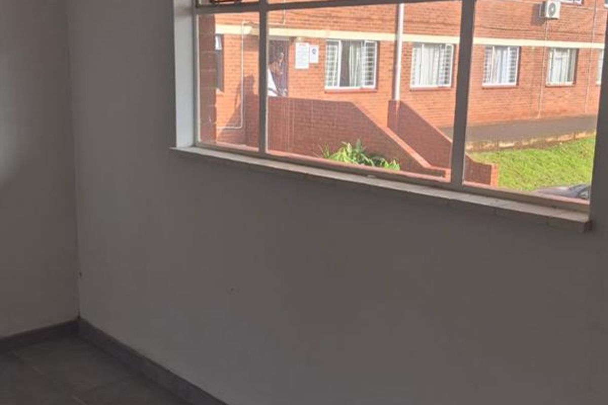 An empty living area featuring tiled flooring and a large window providing natural light and views of the surrounding apartment complex.