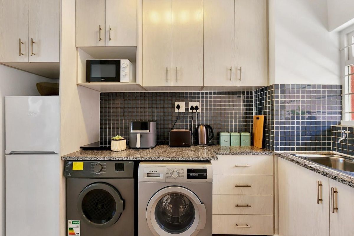 A functional kitchen featuring light wood-finish cabinetry, granite countertops, a dark tiled backsplash, and integrated space for laundry appliances.