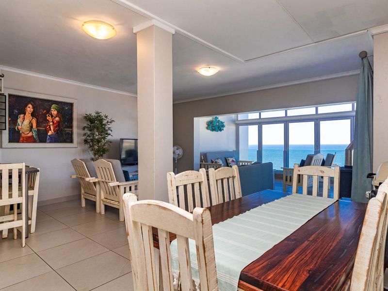 Spacious open-plan living and dining area featuring tiled floors, a structural column, and large sliding glass doors offering expansive ocean views.