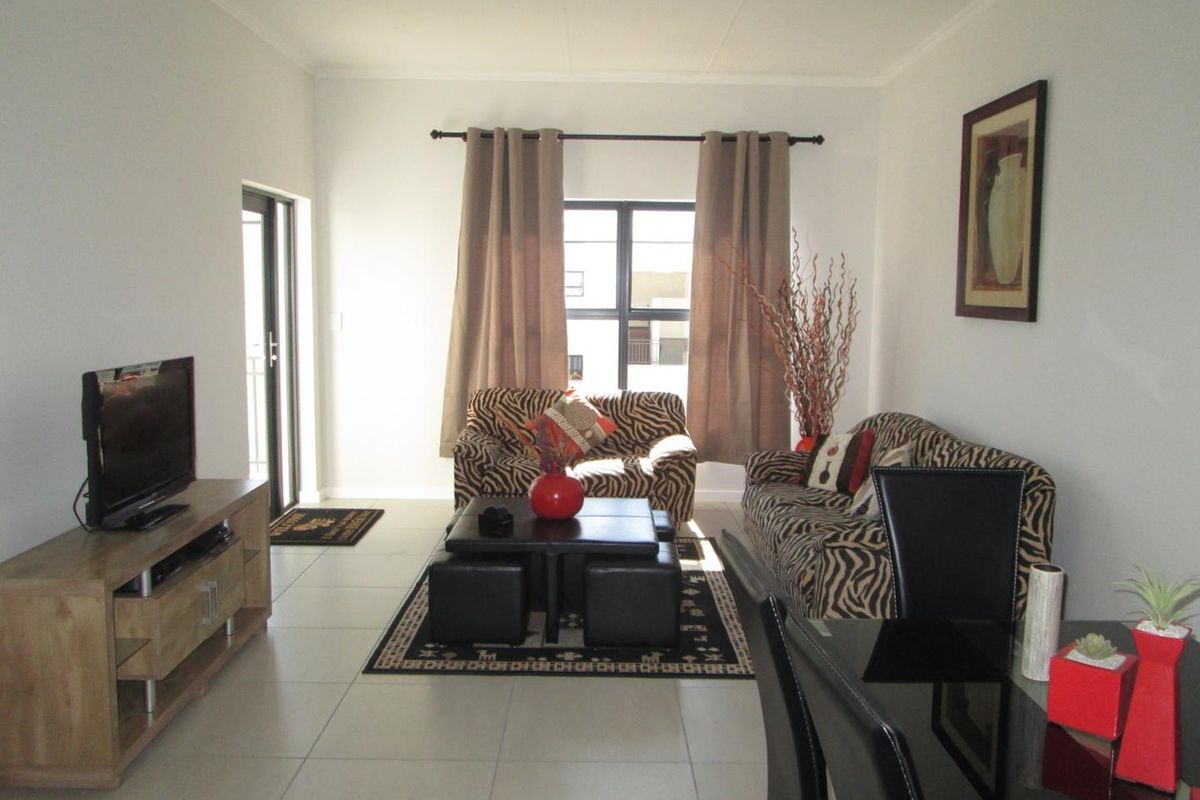 A bright living room featuring neutral tiled flooring and a sliding door providing access to an outdoor area.