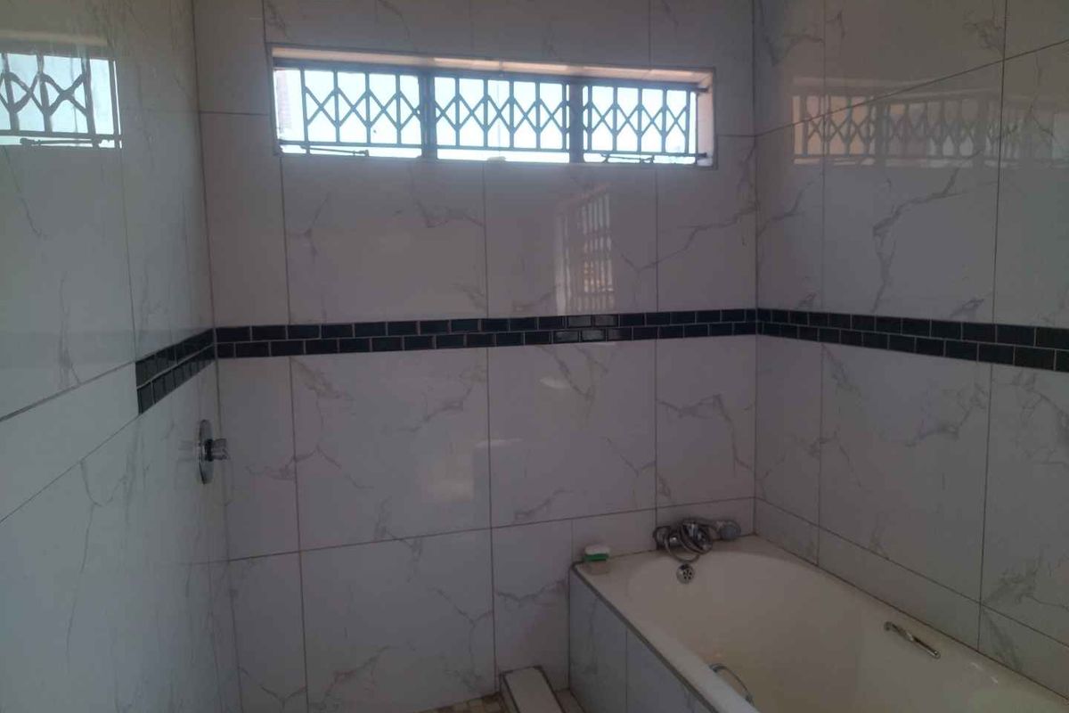 A functional bathroom featuring a built-in bathtub, overhead shower, and marble-effect wall tiling with a decorative border.