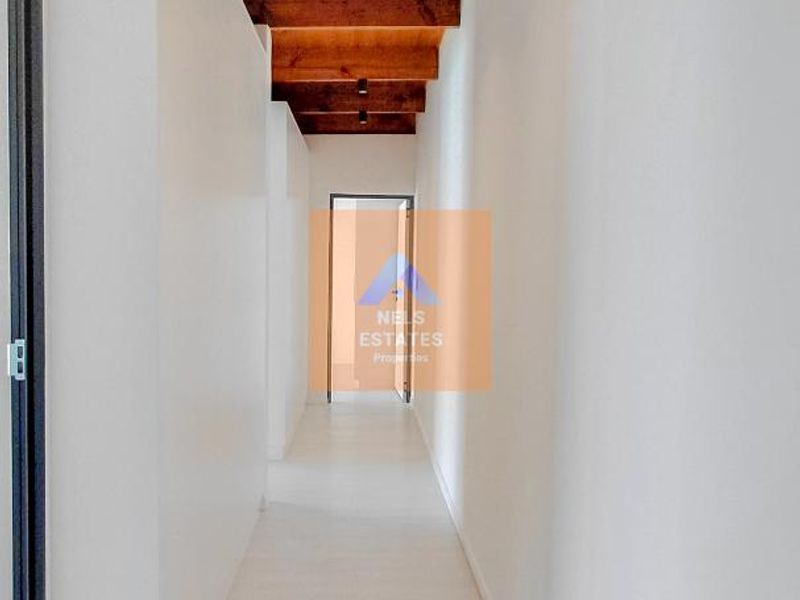 A bright, modern hallway featuring exposed timber ceiling beams, recessed downlighting, and clean, neutral finishes throughout.