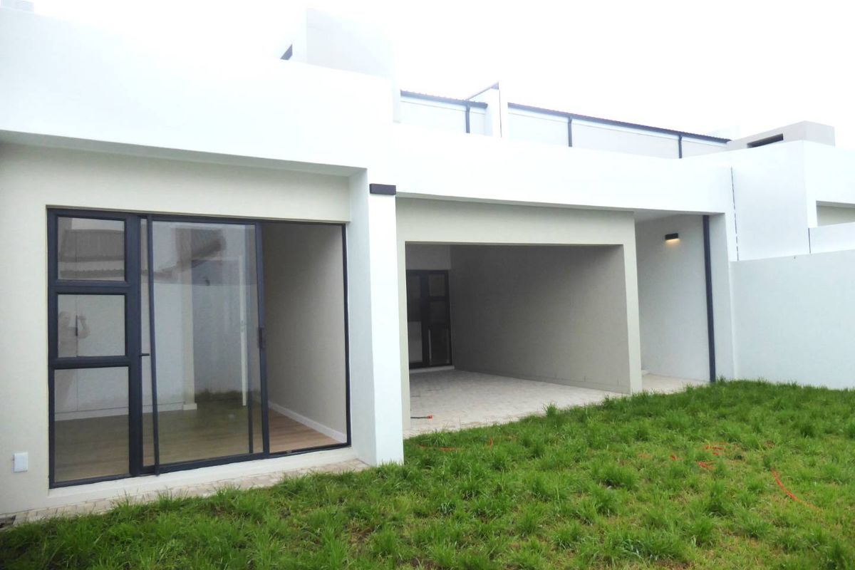 Modern rear exterior featuring a covered patio, large sliding glass doors, and a rooftop terrace with a glass balustrade overlooking the garden.