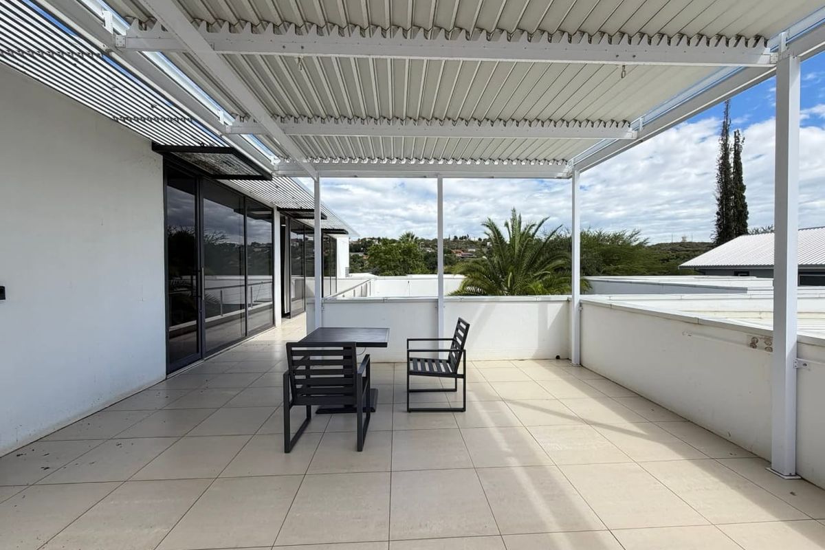 Spacious outdoor balcony featuring a modern louvre roof system, tiled flooring, and large sliding glass doors providing seamless indoor-outdoor flow.
