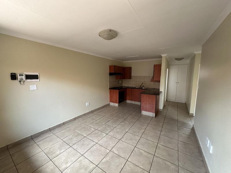 An open-plan living and kitchen area featuring tiled flooring, built-in cabinetry with laminate countertops, and integrated kitchen appliances.