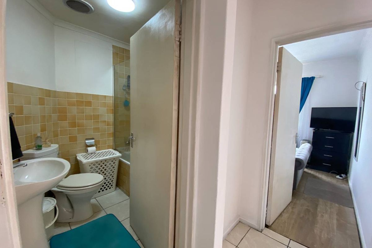 A functional bathroom featuring a pedestal basin, toilet, and shower-over-bath combination, with a view into the adjacent bedroom.