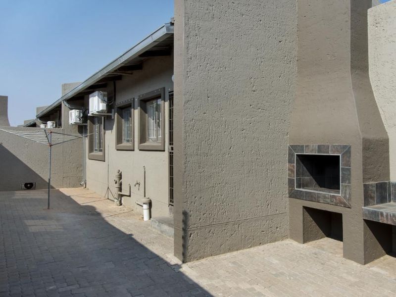 A paved rear courtyard featuring a built-in braai with tiled counter, external air conditioning units, and secure window bars.
