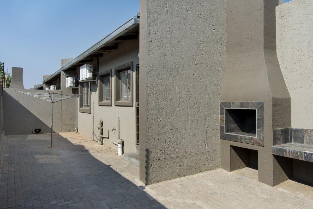 A paved rear courtyard featuring a built-in braai with tiled counter, external air conditioning units, and secure window bars.
