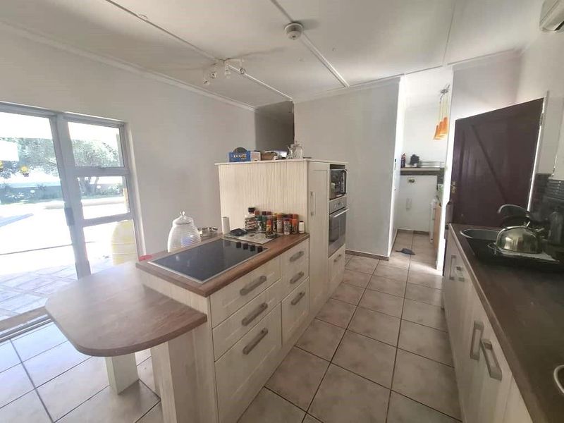 A functional kitchen featuring a central island with a built-in hob, tiled flooring, and direct access to an outdoor patio area.