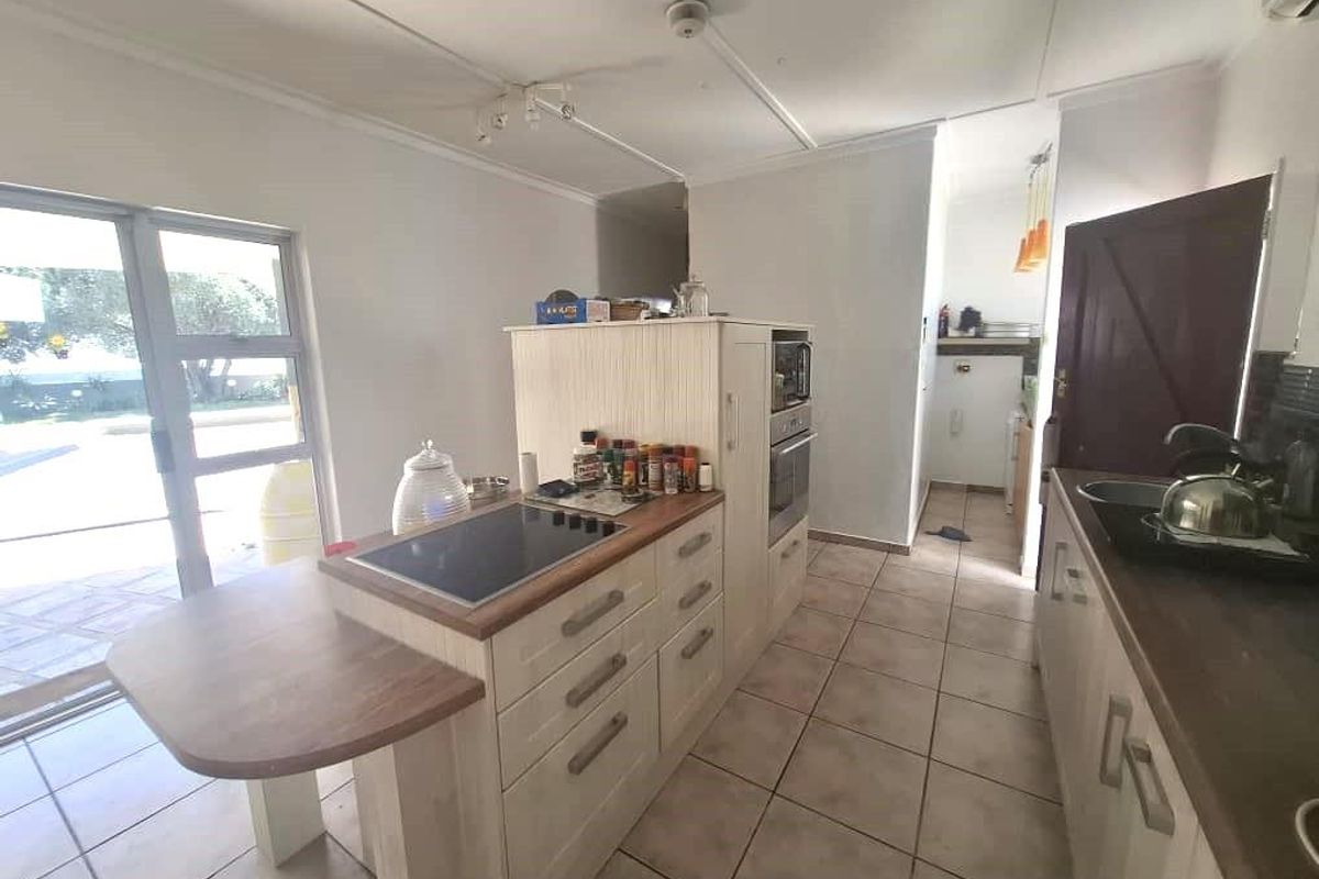 A functional kitchen featuring a central island with a built-in hob, tiled flooring, and direct access to an outdoor patio area.