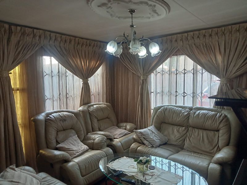 A living room featuring a decorative ceiling rose, a central chandelier, and windows fitted with security gates.