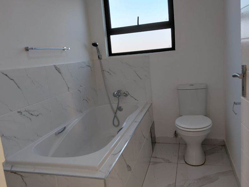 A clean, modern bathroom featuring a built-in bathtub with marble-effect tiling, a handheld shower mixer, and a standard toilet.
