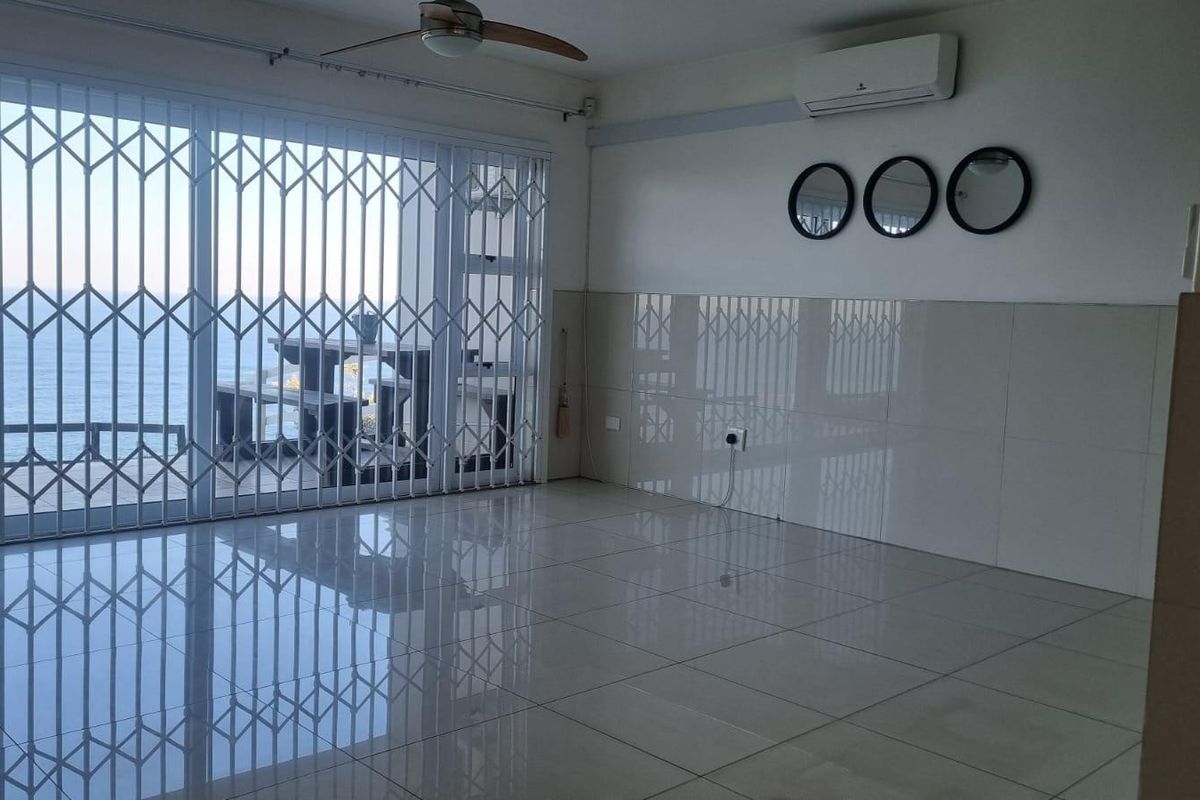 Spacious living area featuring tiled floors, a ceiling fan, split-system air conditioning, and large sliding doors opening to a balcony with ocean views.