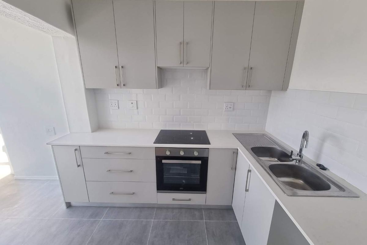 Modern kitchen featuring light grey cabinetry, white subway tile backsplash, stone countertops, integrated electric hob, oven, and a double bowl stainless steel sink.