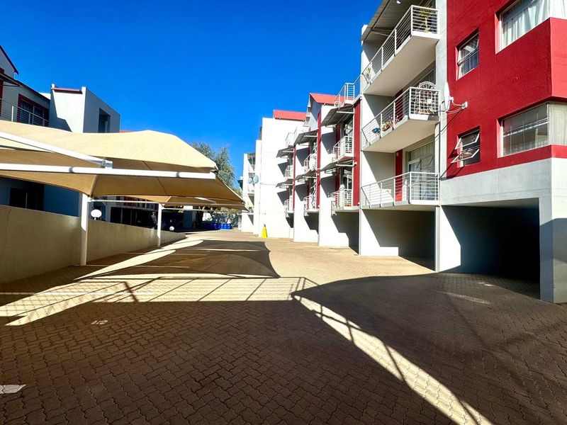 Exterior view of an apartment complex featuring a paved parking area with shade sails and multi-level residential units with private balconies.