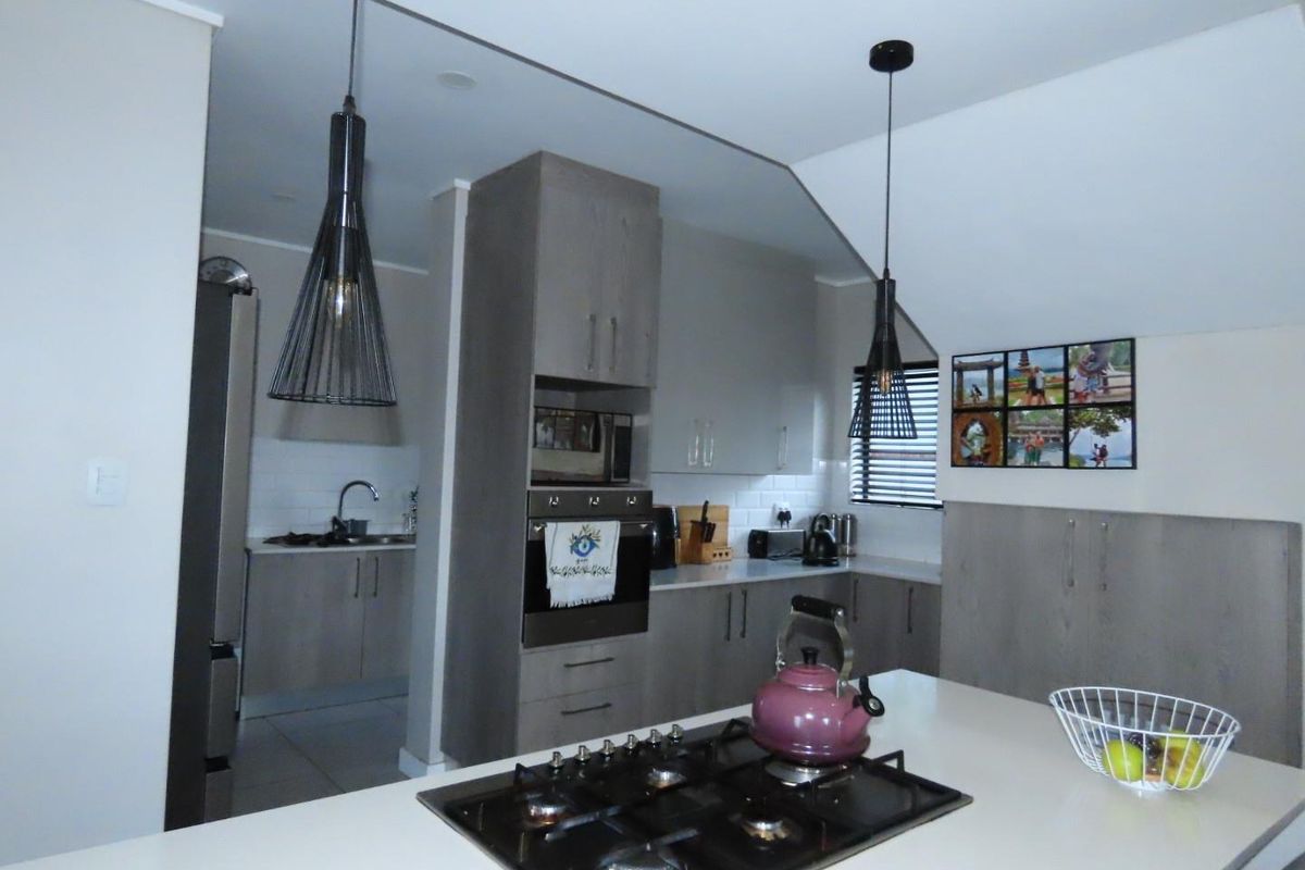 Modern kitchen featuring a central island with a built-in gas hob, sleek cabinetry, subway tile backsplash, and integrated oven, with an adjacent scullery area.