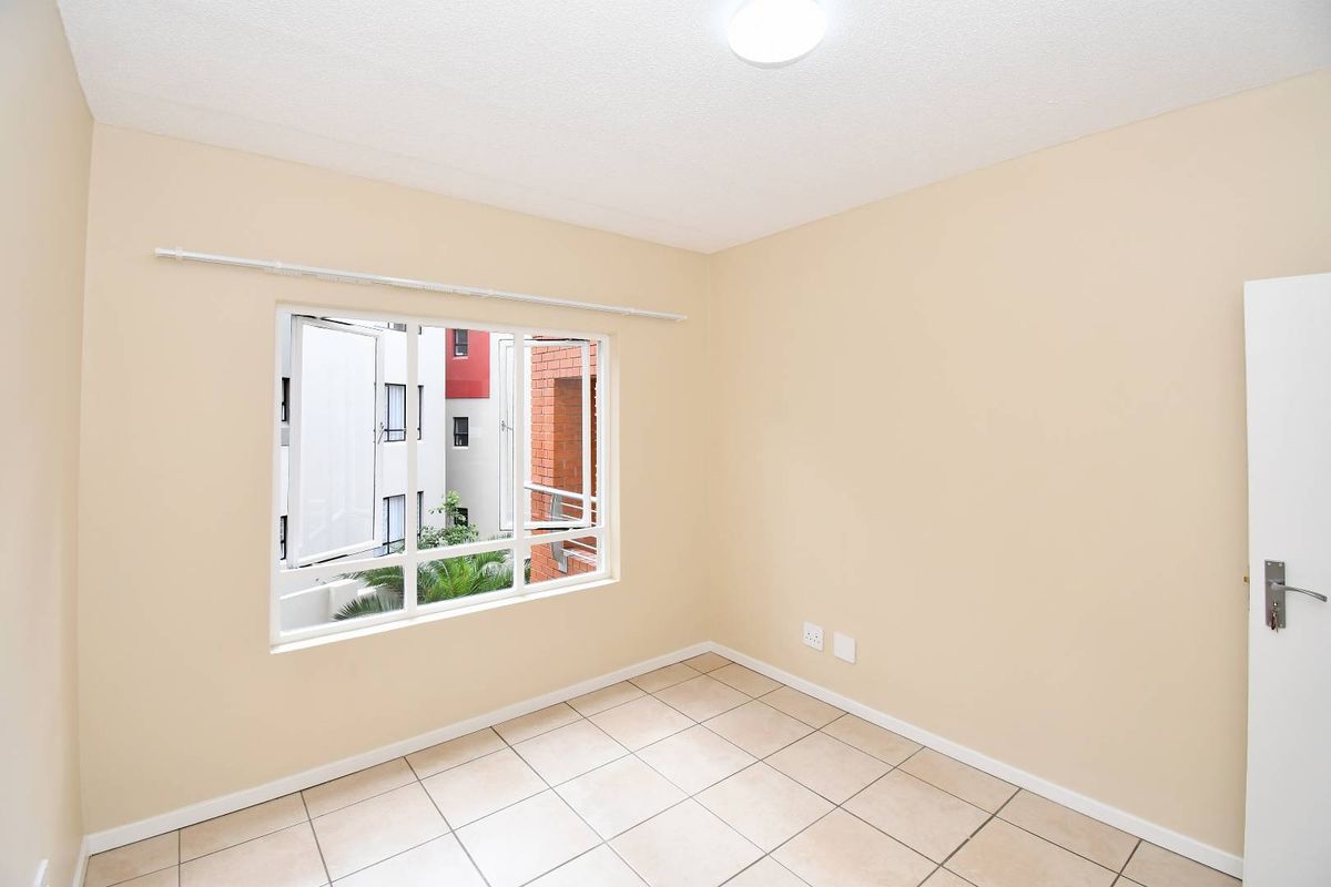 A bright, empty bedroom featuring neutral tiled flooring, a large window with exterior views, and a standard interior door.