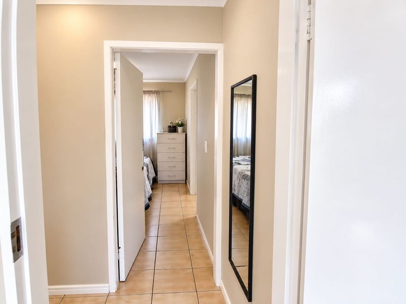 A neutral-toned hallway featuring tiled flooring, connecting to a bedroom area with natural light.