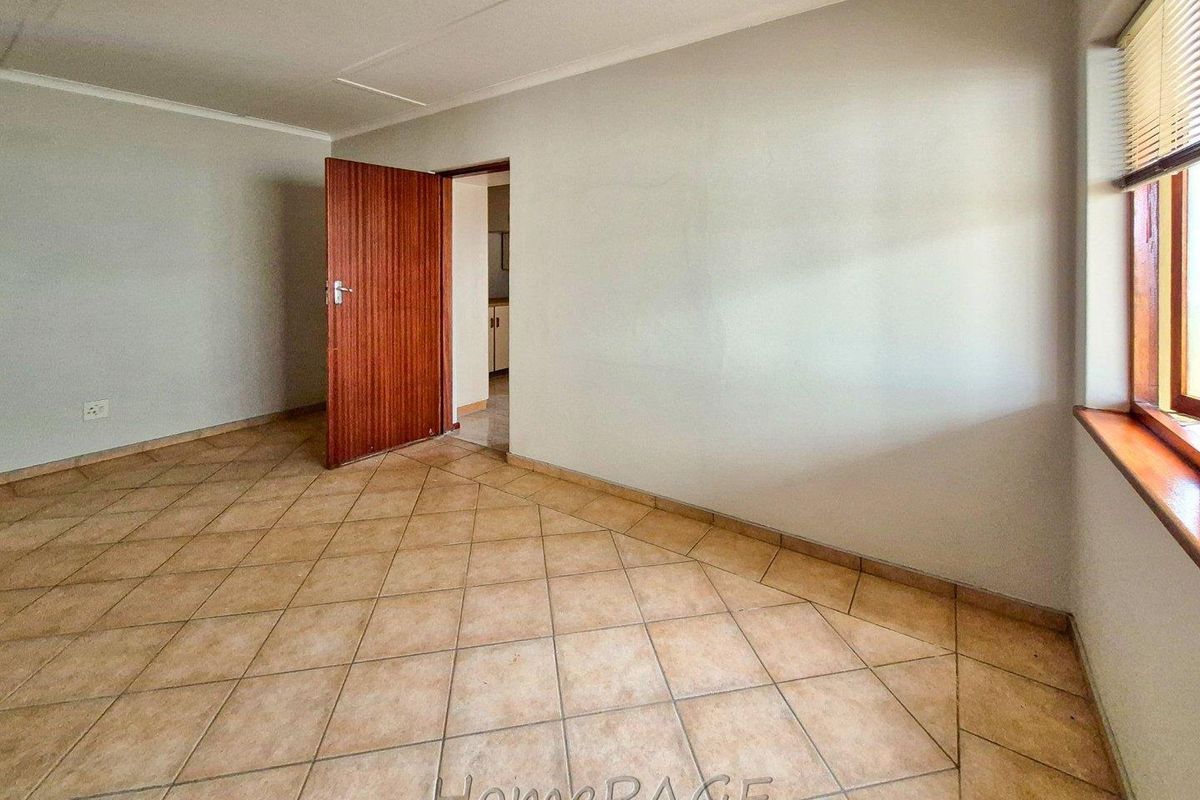 An empty, neutral-toned room featuring tiled flooring, a wooden door, and a window with blinds, suitable for various retail or office uses.