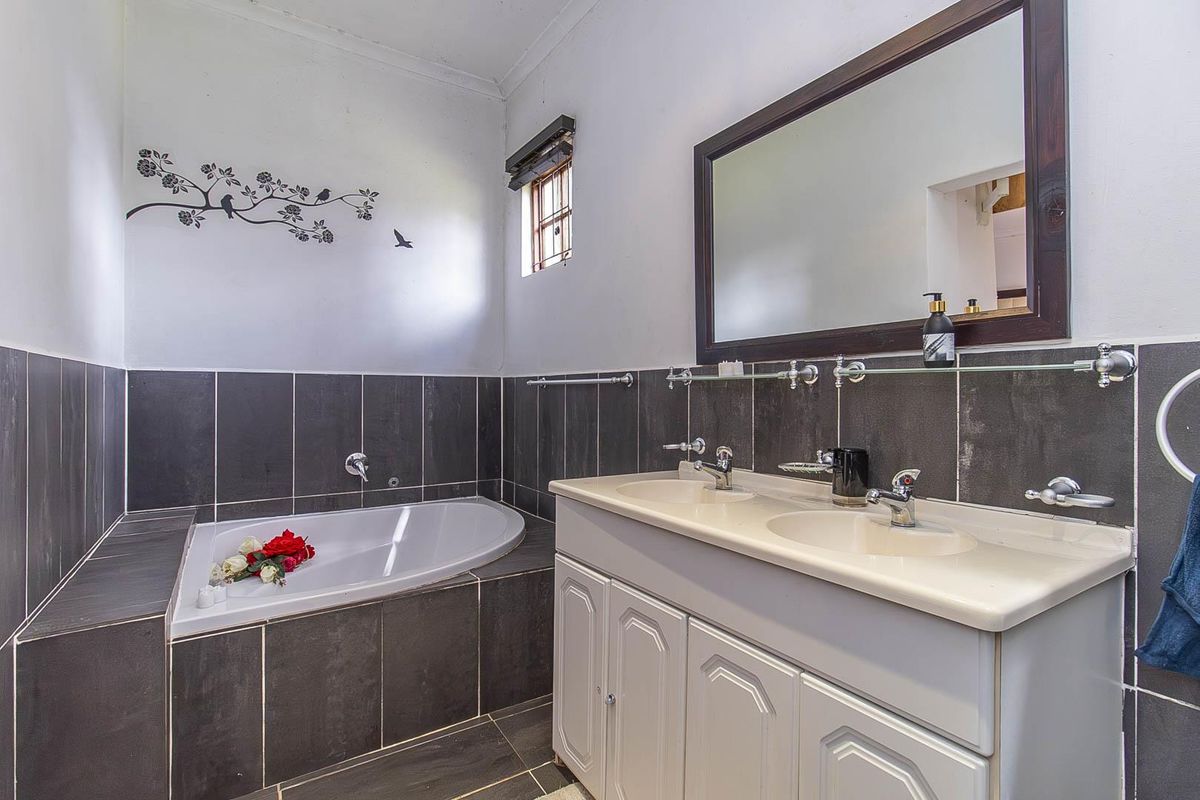 A bathroom featuring a built-in corner bathtub, a double vanity with integrated sinks, and dark tiled wall accents.
