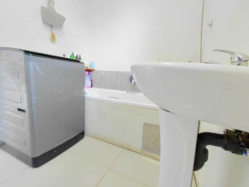 A functional bathroom featuring a bathtub, pedestal basin, and tiled finishes, currently showing signs of wear and exposed plumbing.
