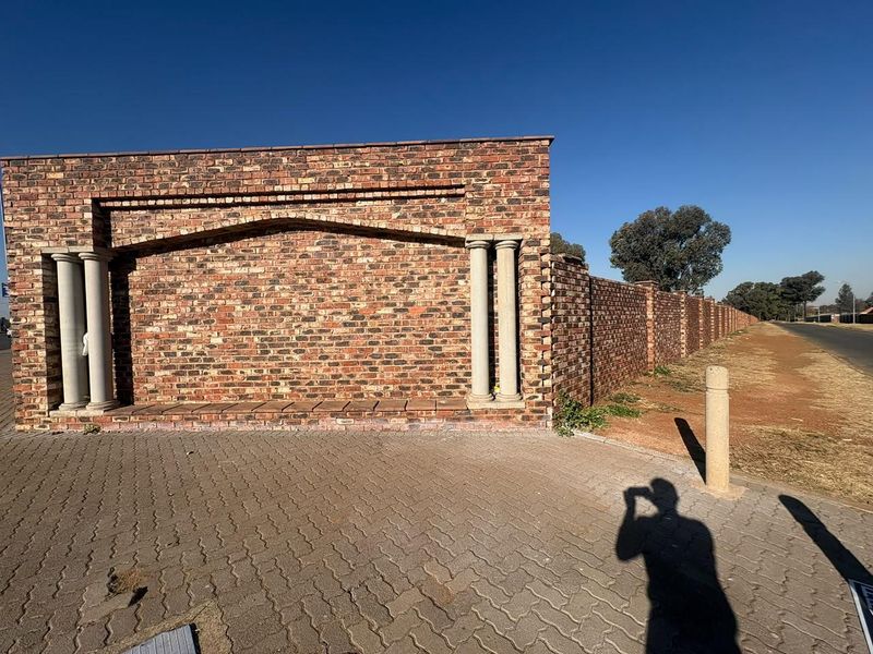 A view of the property's front boundary featuring a decorative face brick wall with stone columns and a paved driveway entrance.