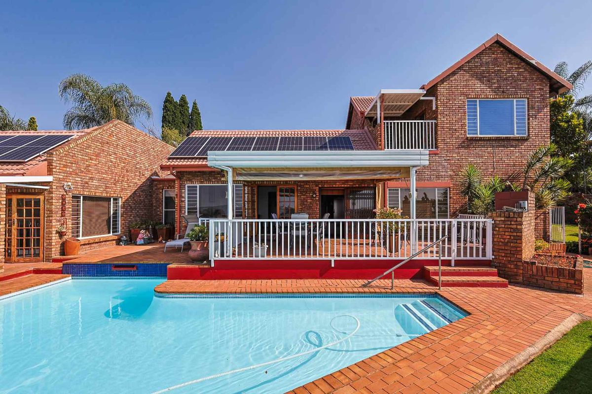 Rear view of the house featuring a swimming pool, paved patio area, and solar panels installed on the roof.
