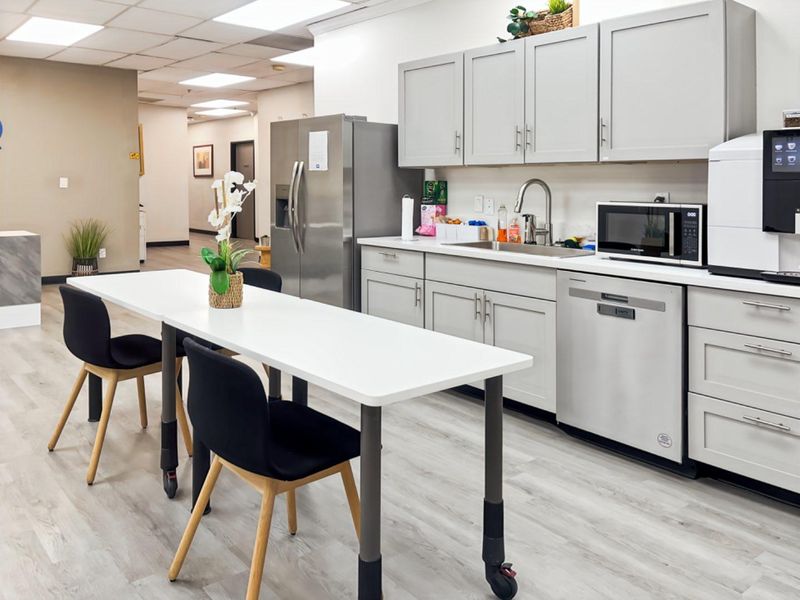 A modern office kitchenette featuring light grey cabinetry, stainless steel appliances, and durable wood-look flooring, providing a functional break area for staff.