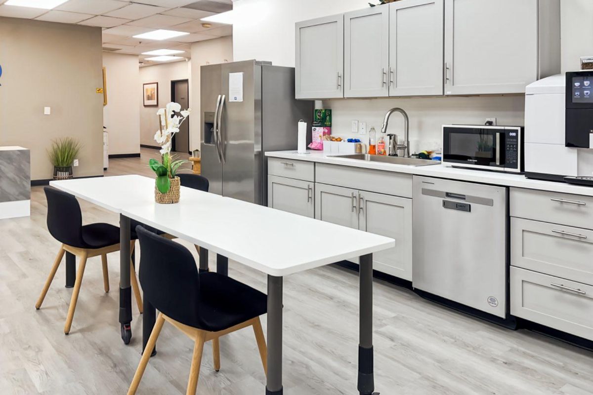 A modern office kitchenette featuring light grey cabinetry, stainless steel appliances, and durable wood-look flooring, providing a functional break area for staff.