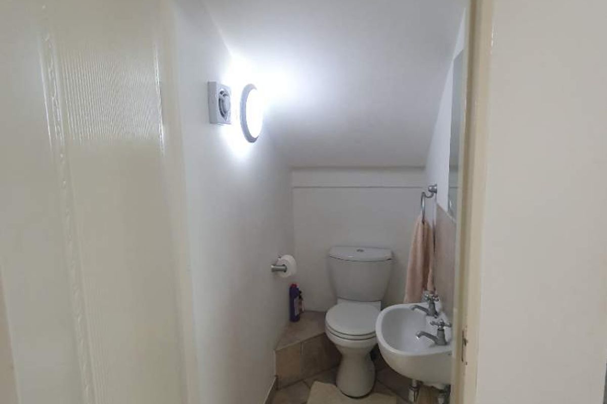 A compact guest bathroom featuring a toilet and wall-mounted basin with tiled flooring, located under a sloped ceiling.