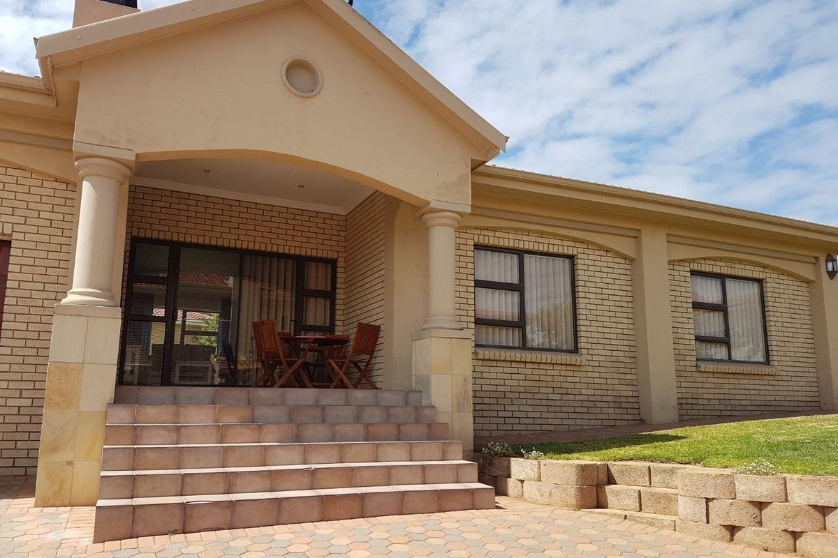 A well-maintained rear exterior view featuring a covered patio with tiled steps, brick facade, and a landscaped garden with retaining walls.