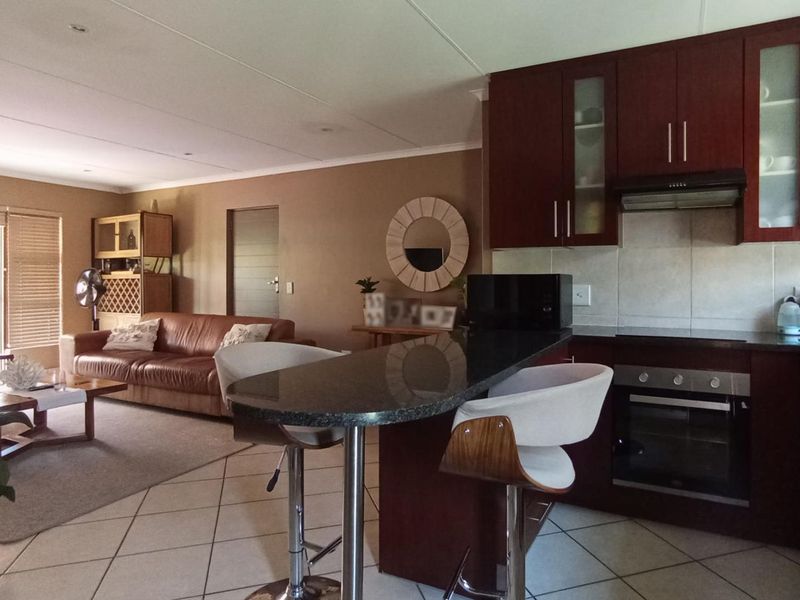 Open-plan living and kitchen area featuring dark wood cabinetry, granite breakfast bar, built-in oven, and tiled flooring throughout.