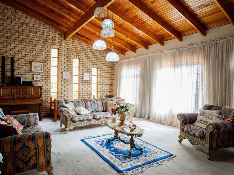 Spacious living room featuring a high exposed timber beam ceiling, exposed brick feature wall, and large windows allowing for ample natural light.