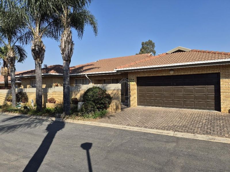 Front elevation of a townhouse featuring a brick facade, tiled roof, paved driveway, and a double garage door with secure gated access.