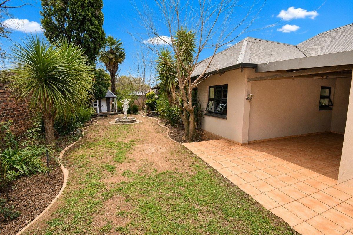 A rear view of the property featuring a covered tiled patio area, a landscaped garden with a central fountain, and a brick boundary wall.
