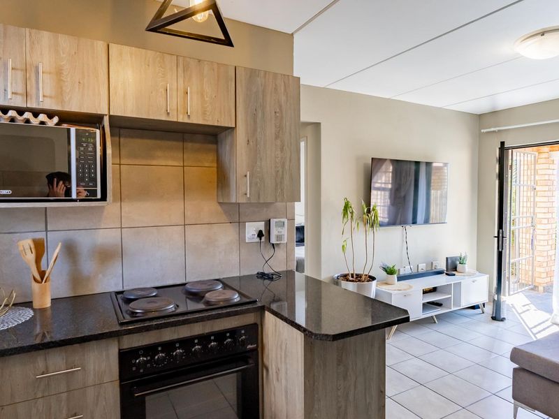 Open-plan kitchen and living area featuring modern wood-finish cabinetry, granite countertops, electric stove, and direct access to an outdoor patio area.