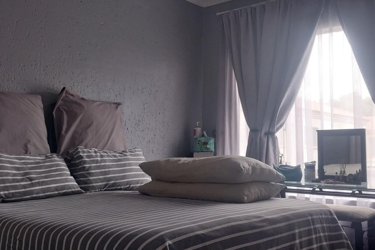 A cozy bedroom featuring textured grey walls and a window with curtains, providing natural light and a comfortable atmosphere.