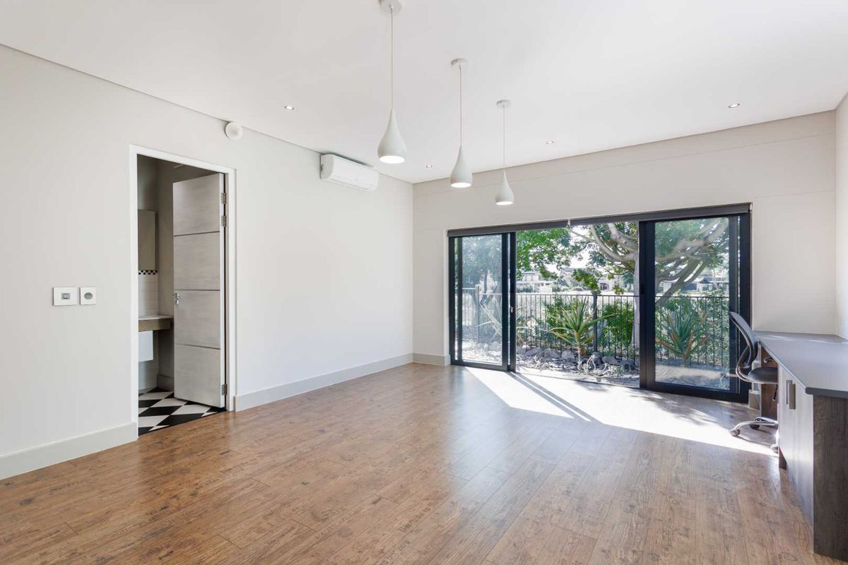 Spacious bedroom featuring wood-look laminate flooring, built-in desk, split-system air conditioning, and sliding glass doors leading to an outdoor area with an en-suite bathroom.