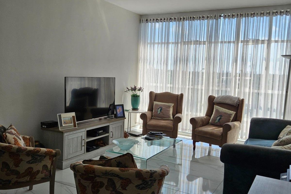 A bright living room featuring large floor-to-ceiling windows that provide ample natural light and polished tiled flooring throughout.
